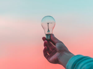 photo of a hand holding a translucent lightbulb with a sunset in the background 