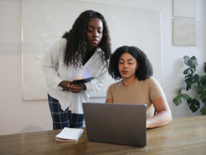 photo of two young Black women working together at a laptop computer