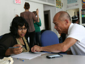 photo of a man teaching a woman something with paper and pen at a table