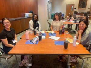 candid photo of a diverse group of seven adults seated at tables with ARL-branded folders and cups