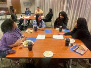 photo of diverse group of eight adults sitting around two tables talking and smiling