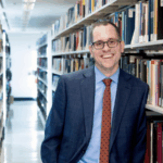 photo of Jon Stroop standing in the library stacks and smiling